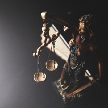 A symbolic statue representing justice, holding scales, against a dark background.